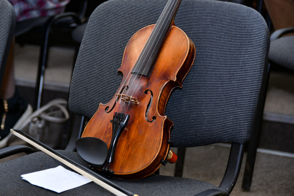 A violin with a bow and notes stands on a chair in the middle of an empty concert hall.